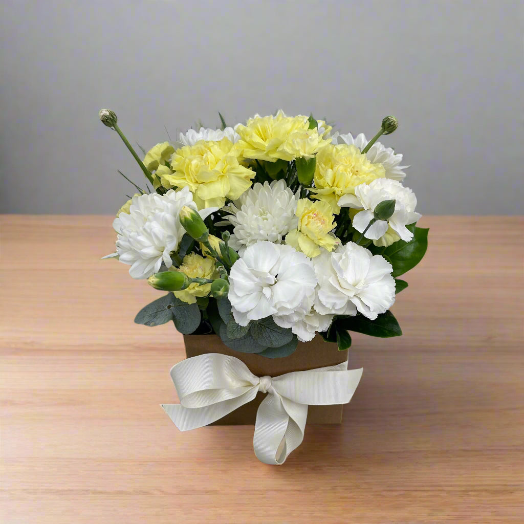Box arrangement with yellow and white flowers on wooden table