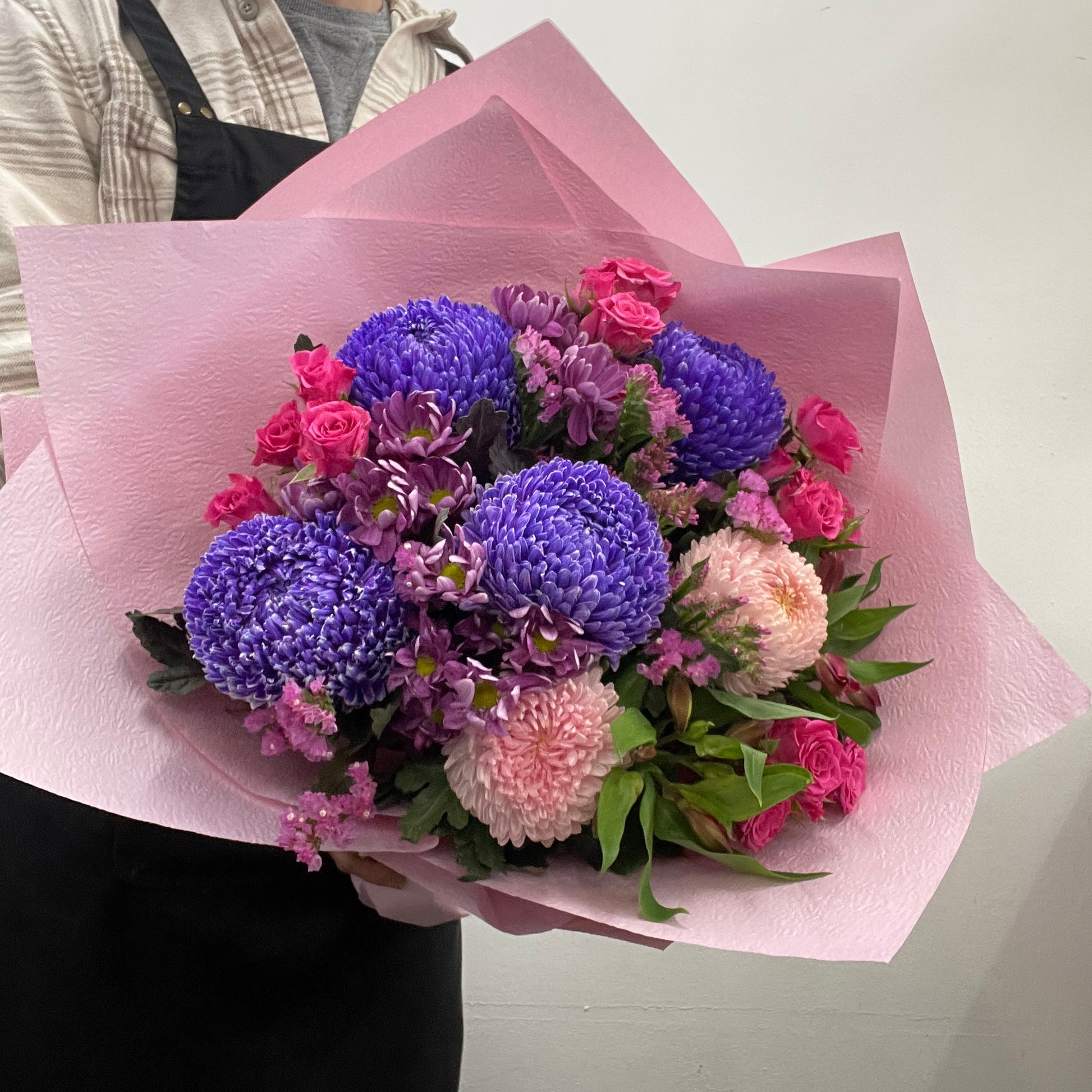 Bouquet of flowers wrapped in pink paper held by a person.