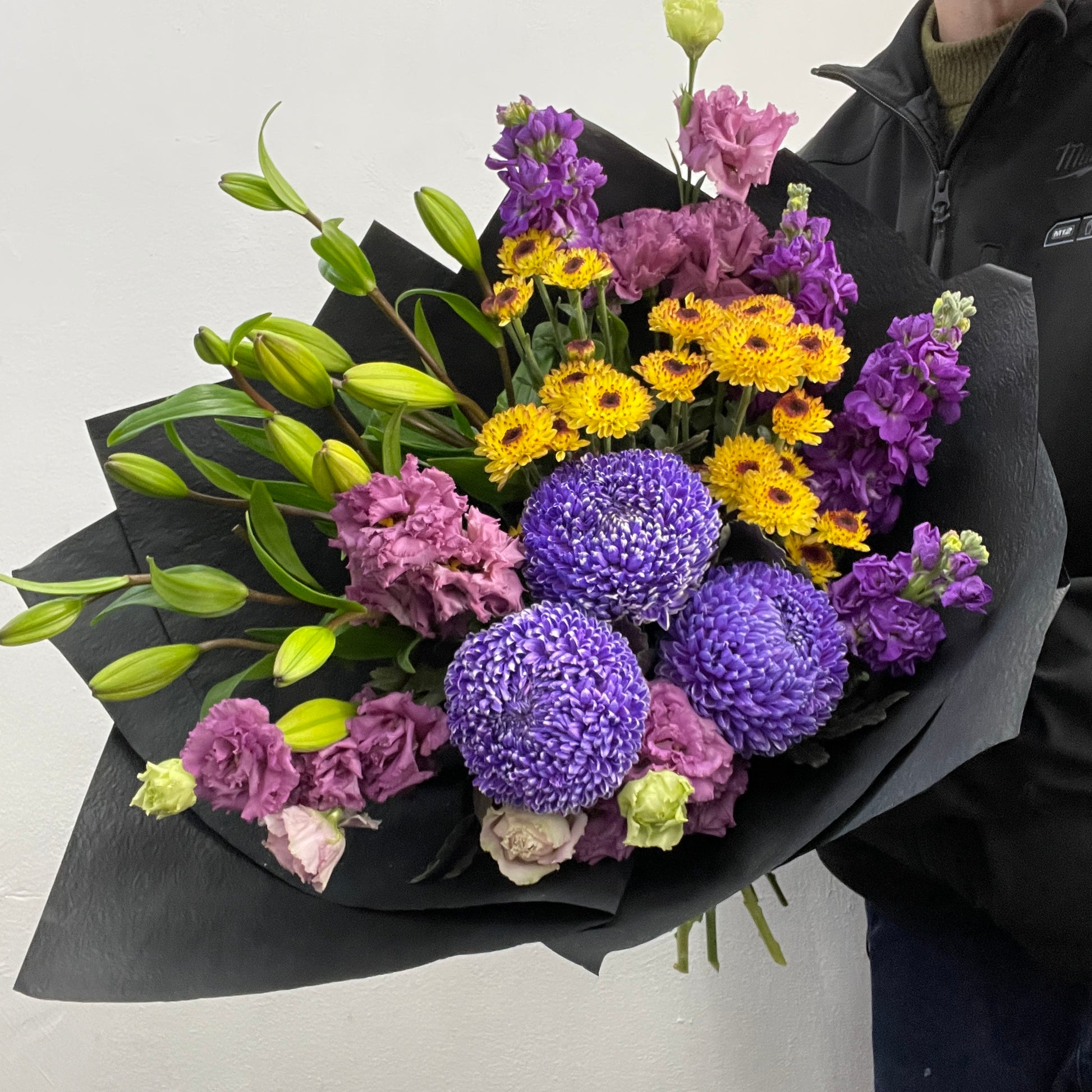 Bouquet of purple and yellow flowers held by a person against a light background