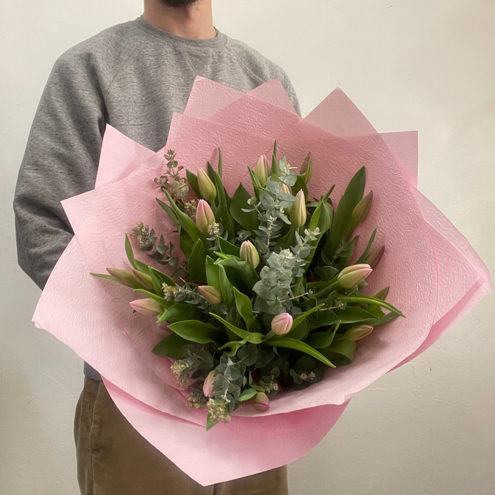 Rounded bouquet of pink tulips in pink paper with green eucalyptus, made by Adam The Flower Man in Sandringham.