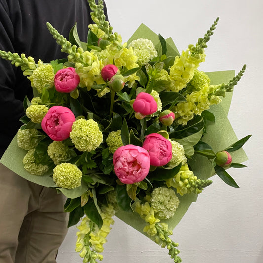 Spring bouquet featuring Coral Charm pink peonies, yellow snapdragons, and green viburnum snowball, made by Adam The Flower Man in Sandringham.