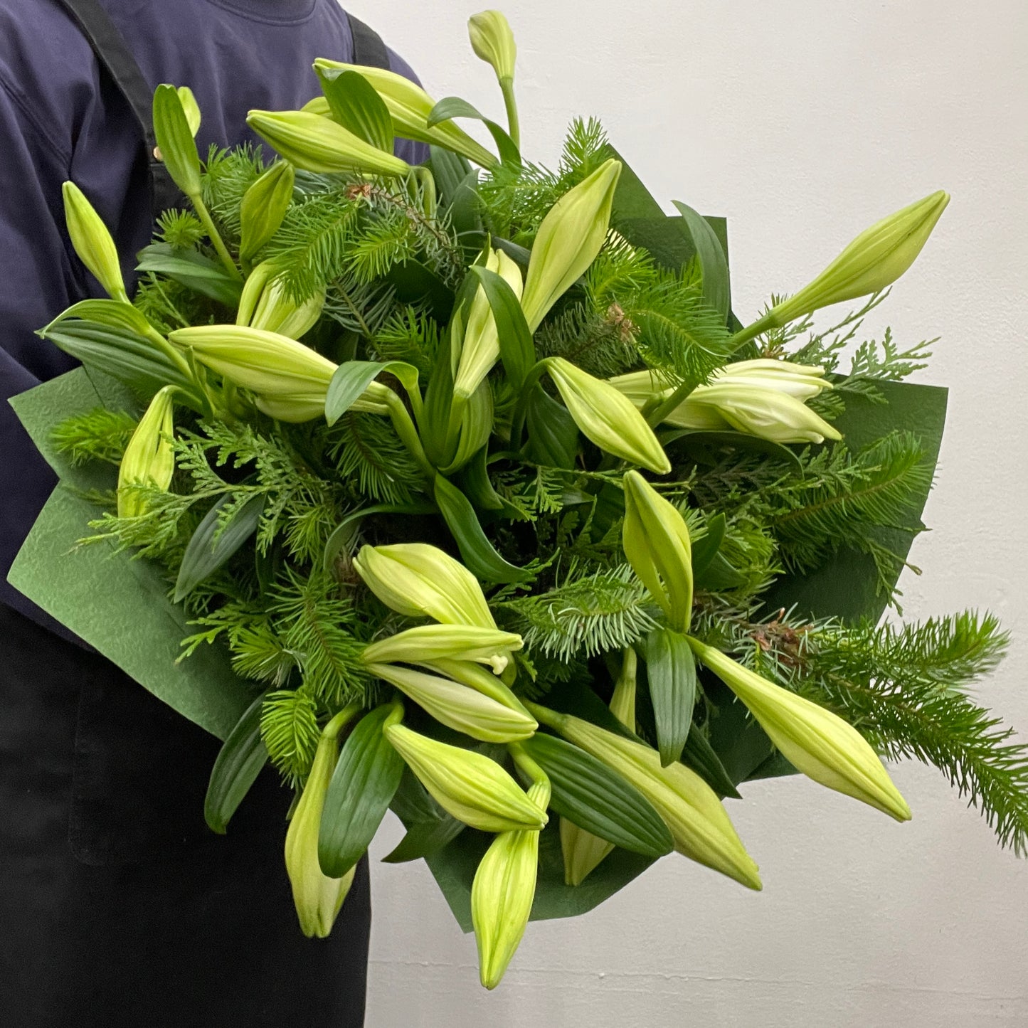 Christmas bouquet featuring white Christmas lilies with spruce and cypress foliage, wrapped and styled for the holiday season.