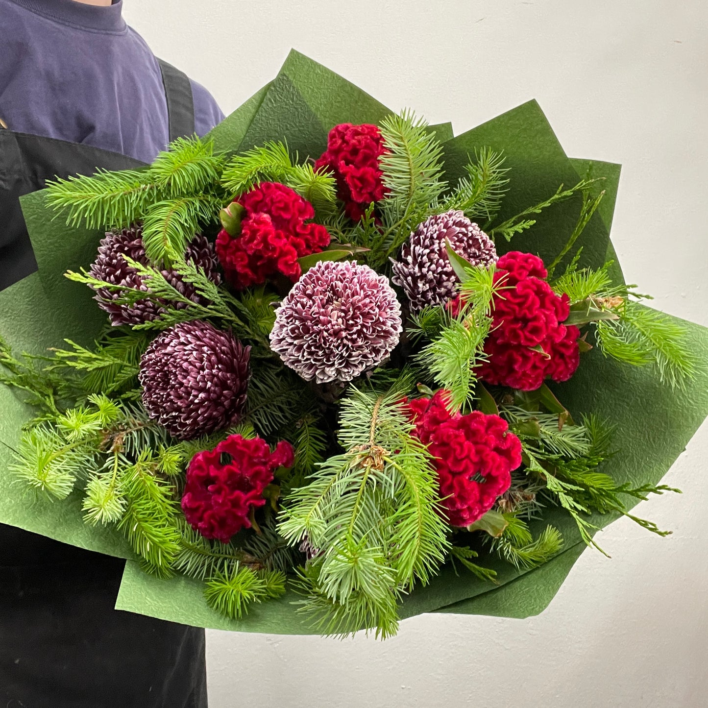 Christmas bouquet with celosia brains, disbuds, and Christmas foliage, wrapped and styled for the holiday season.
