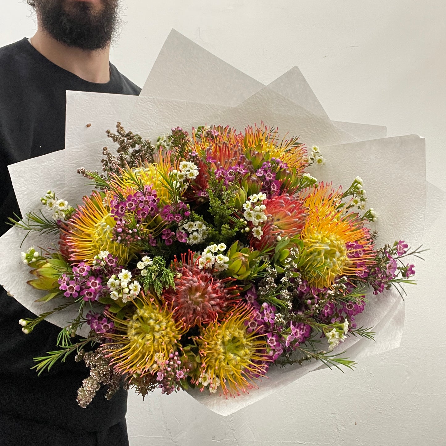 Rounded bouquet featuring native pincushions in orange and yellow tones with colourful foliage, part of the Spring Limited Collection 2025 by Adam The Flower Man.