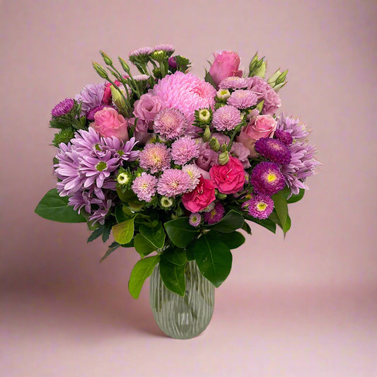 Pink seasonal flower bouquet wrapped in signature paper and ribbon, featuring fresh summer blooms.