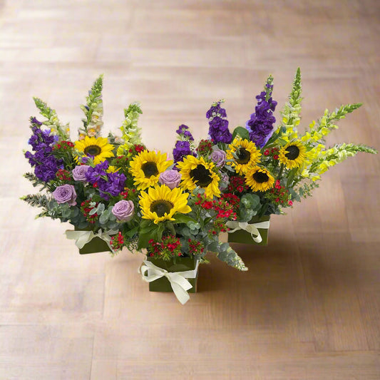 Box arrangement with mixed seasonal flowers in yellow, red, and purple tones.