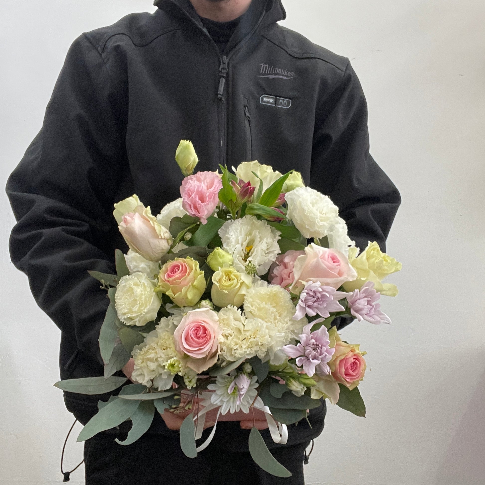Person holding a arrangement  of flowers against a plain background