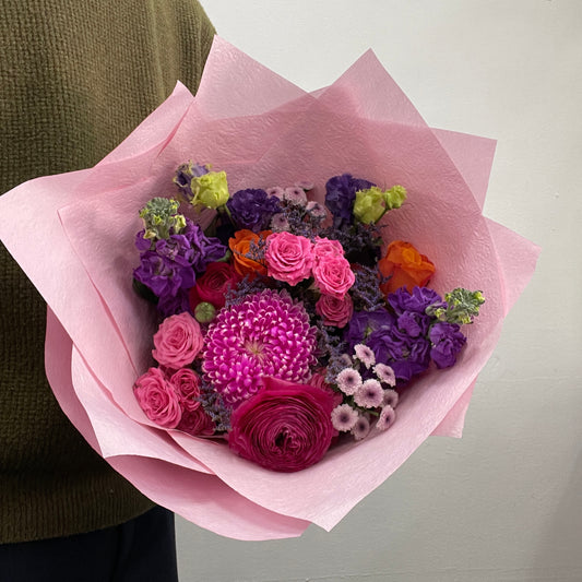 Bouquet of flowers wrapped in pink paper held by a person.