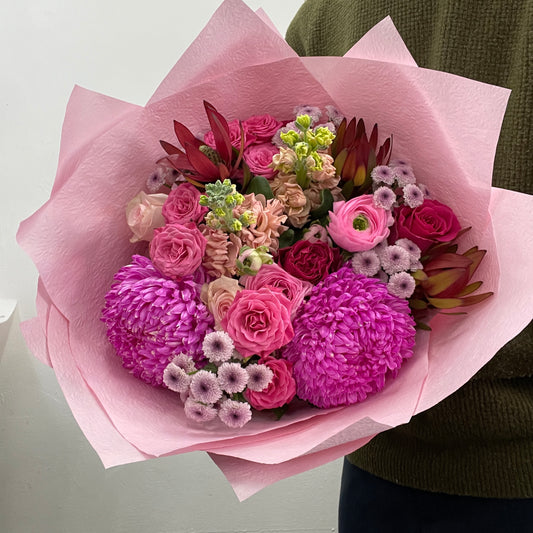 Bouquet of flowers wrapped in pink paper held by a person wearing a green sweater.