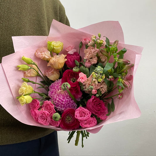 Bouquet of flowers wrapped in pink paper held by a person wearing a green sweater.