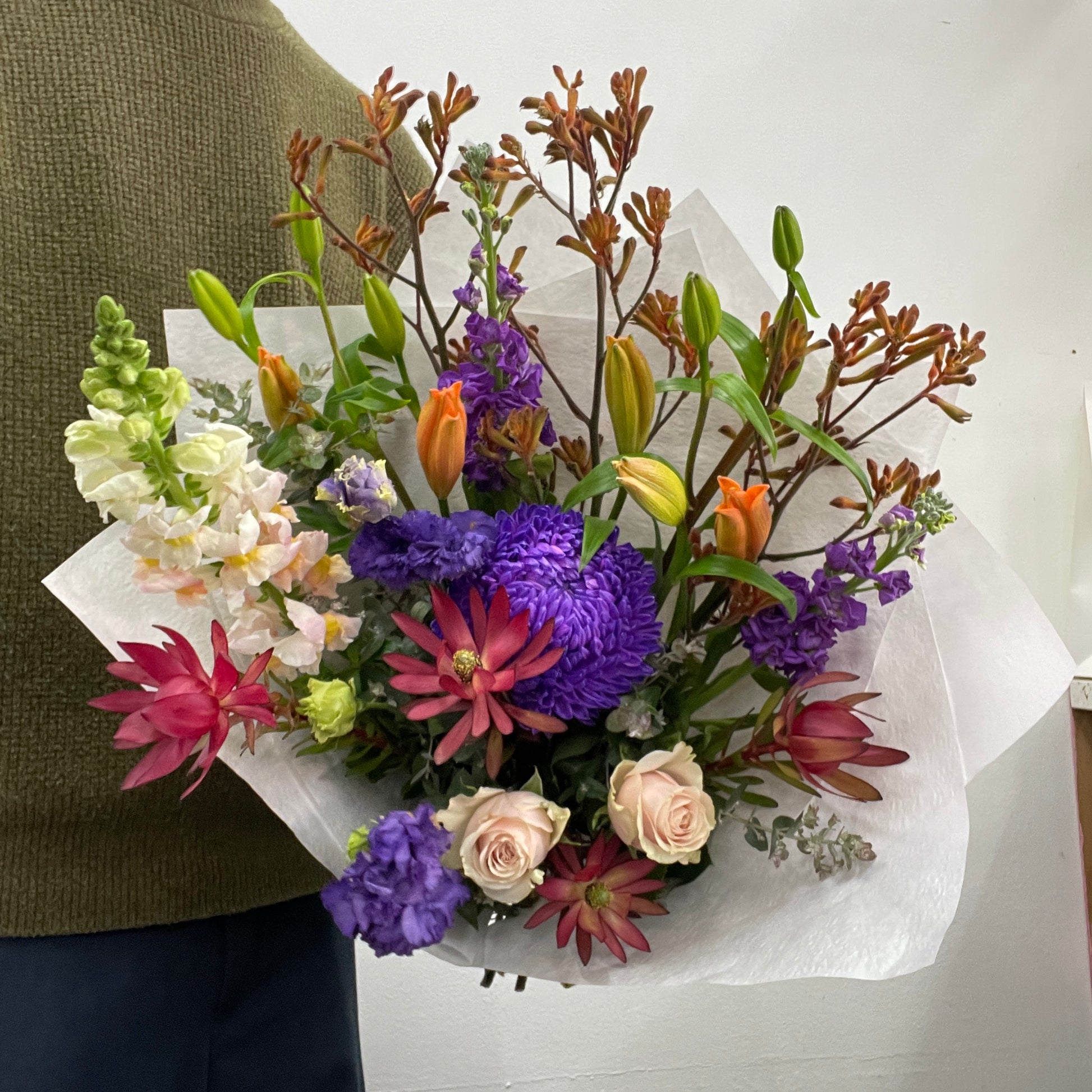 Bouquet of colorful flowers wrapped in white paper held by a person.