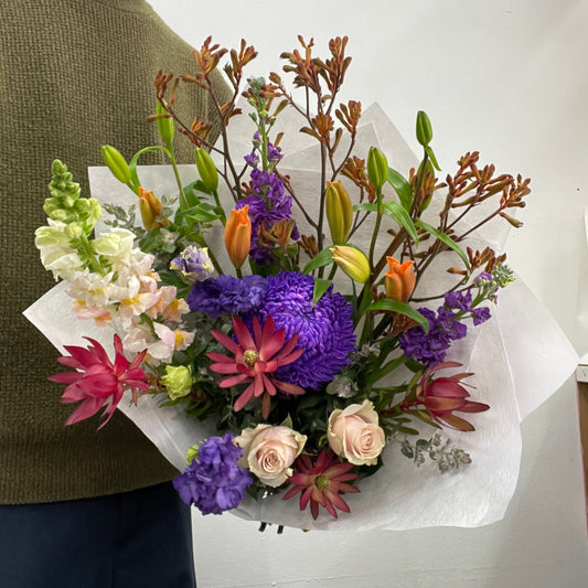 Bouquet of colorful flowers wrapped in white paper held by a person.