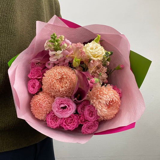 Bouquet of flowers wrapped in pink paper held by a person wearing a green sweater.