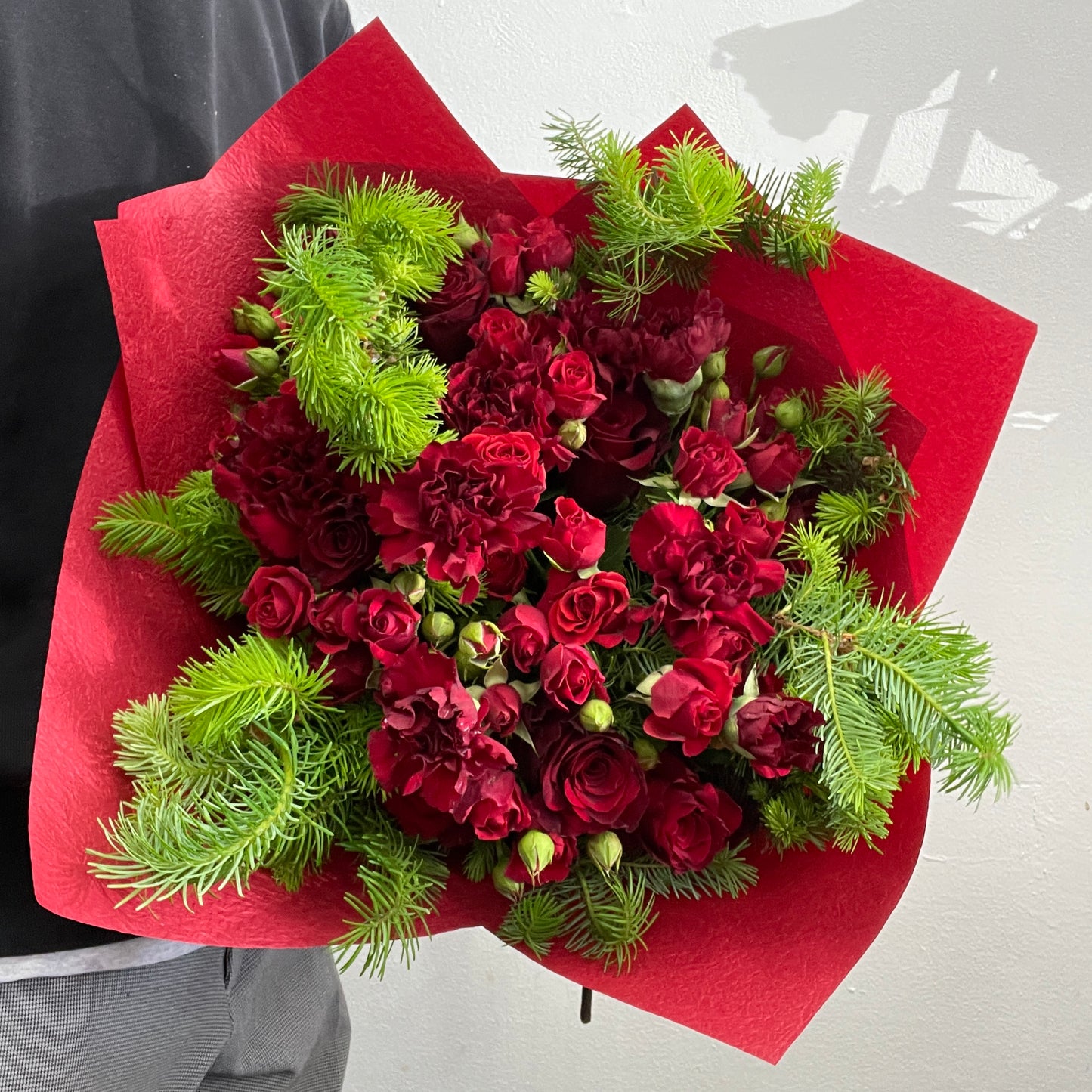 Rounded Christmas bouquet featuring red roses, red spray roses, red carnations, and spruce, part of the Christmas Collection by Adam The Flower Man.