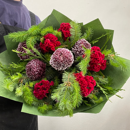 Christmas bouquet with celosia brains, disbuds, and Christmas foliage, wrapped and styled for the holiday season.