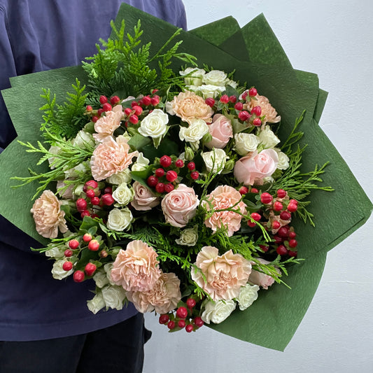Blush Christmas bouquet with blush roses, white and red accents, hypericum berries and festive foliage.