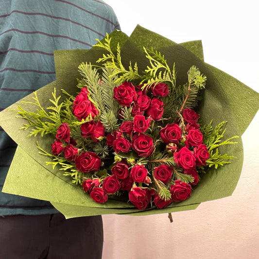Red and green Christmas bouquet with red roses, spray roses and festive foliage.
